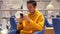 Young man in a yellow hoodie sits in a cafe mall shopping center and uses a modern smartphone