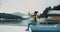 Young man in a yellow jacket and red hat taking pictures by the way he is sitting on a blue boat in the middle of