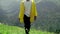 A young man in a yellow raincoat climbs the slope and enjoys the magnificent scenery of the mountainous areas. Tourism