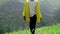A young man in a yellow raincoat climbs the slope and enjoys the magnificent scenery of the mountainous areas. Tourism