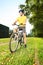 Young man in yellow shirt standing on a bike in a park