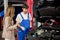 Young mechanic talking to customer asian woman about car with repairing in garage, auto service.