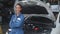 Young mechanic woman standing smiling with car in the garage, technician maintenance vehicle and emotion happy.