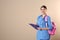 Young medical student with clipboard and backpack on color background.