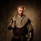Young medieval knight posing on dark background.
