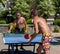 A young men plays table tennis without shirts in a park on a background of palms in a tourist city.