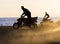 Young men on quad bikes on sandy beach during sunset