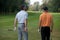 Young men standing in golf course with sticks, rear view