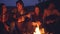 Young men and women are singing songs to the guitar resting around campfire and enjoying music and good company on
