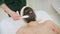 Young metrosexual man applying charcoal clay facial mask in beauty Spa. Handsome shirtless guy cleaning face skin