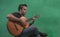 Young mexican with dark skin, latin playing guitar on green background