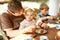 Young middle-aged father feeding cute little toddler girl in restaurant. Kid boy eating on background. Happy healthy