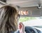 A young middle-aged woman does make-up paints her lips with lipstick in the car while looking into a small mirror in a visor