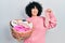 Young middle east woman holding laundry basket and sock smiling looking to the side and staring away thinking