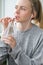 Young millennial blonde woman drinking water from eco bottle with metal reusable straw tube and doing yoga exercise