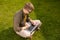 Young millennial man sits on grass remotely works on laptop, freelance lifestyle