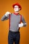 Young mime looking at side in vest and red hat Isolated on orange background