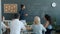 Young mixed race man making report pointing at chalkboard and talking to milti-ethnic group of colleagues