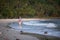 Young mixed-race woman walks along a polluted tropical beach.