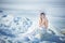 Young model in luxurious strapless corset ball gown sitting on slabs of broken ice at the frosty seaside. Winter