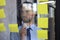 Young modern business man using adhesive notes while standing behind the glass wall in the office