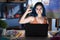 Young modern girl with blue hair sitting at art studio with laptop at night smiling positive doing ok sign with hand and fingers