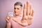 Young modern romantic man holding heart shape drawing over isolated pink background with open hand doing stop sign with serious