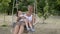 Young mom and baby swing and play sitting on a hanging swing in the Park. The child sits on her mother`s lap, they smile