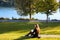 Young mother in black sitting on green lawn outside  and breastfeeding her baby on public