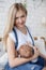 Young mother breastfeeding a child sitting on a bed in a bright bedroom