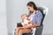Young mother brestfeeding her newborn child sitting in vintage armchair. White walls on background. Mom nursing baby