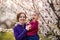 Young mother and child daughter together, hugging and laughing in a Flowering apricot garden. Family outdoors lifestyle