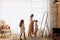 Young mother combing her little daughter`s hair standing in front of the mirror and her second daughter comes to them in
