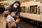 Young mother combs her daughter while they wait for the train at the station. Mother and daughter wearing disposable mask on the