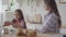 Young mother and cute girl sitting in the kitchen. Little girl takes two Easter eggs and giving one to mom. Preparation