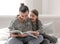 Young mother and daughter have fun together, reading a book at home on the couch