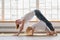 Young mother doing yoga with 3-years daughter in front of window. Happy mom smiling while practicing yoga together with