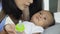 Young mother feeding water to baby on the bed