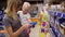 Young mother in glasses holding her child in her arms while choosing cookies on the shelves in the supermarket