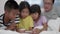 Young mother and her daughters and son are playing mobile phone in bedroom.