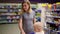 Young mother with her little baby sitting in a grocery cart in a supermarket is pushing the cart forward walking among