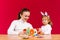 A young mother and her little daughter in bunny ears make decorative handmade textile Easter eggs. Red background and