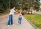 A young mother and her little daughter are dancing in the park. A girl and a woman are circling on the sidewalk