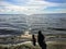 A young mother and her toddler daughter sitting together alone on a sandy beach watching the sparkling lake water