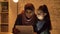 A young mother in a hijab sits with her little daughter on a sofa in the evening and uses a tablet, watch an interesting