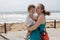 A young mother holds a baby girl in her arms against the background of the sea in a storm, strong wind