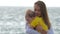 Young mother holds baby in her arms while standing by the sea or ocean.