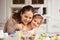 Young mother hugs her little daughter with white rabbit`s ears on her head dyeing the eggs for the Easter table in the