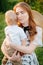 A young mother hugs and soothes her beloved son while sitting on the green lawn.