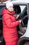 Young mother installing child safety seat on rear chair of car, woman in winter clothes